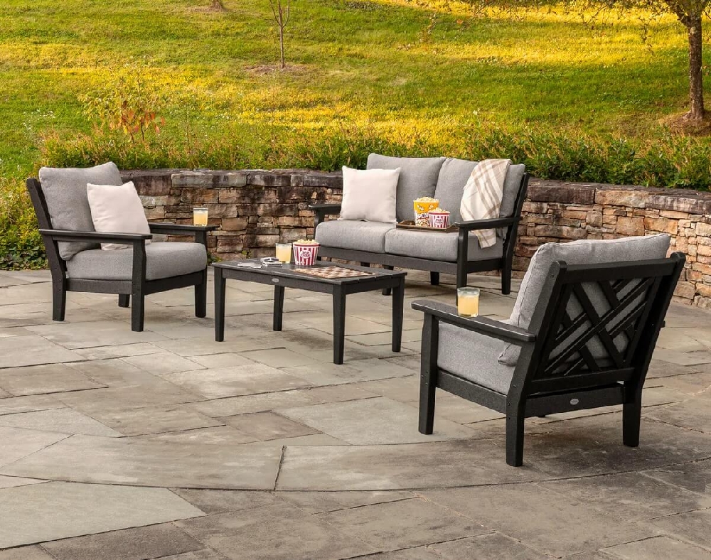Commercial outdoor lounge furniture featuring cushioned club chairs and a sofa arranged around a coffee table on a stone patio.